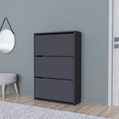 A dark gray shoe cabinet with three flip-down drawers stands against a gray wall. A round mirror hangs on the wall to the left, and a small, light gray stool is partially visible in the foreground.
