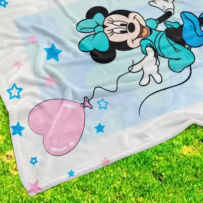 A close-up view of a Minnie Mouse blanket with stars and a heart-shaped balloon, laid out on green grass.