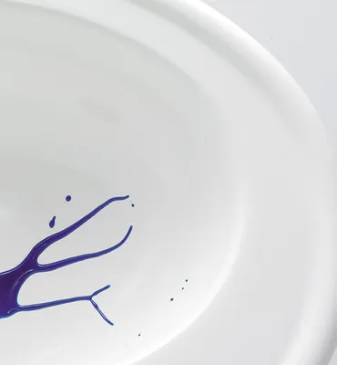 A close-up of a white sink with purple paint splatters.