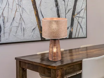 A table lamp is placed on a wooden dining table in front of a painting.