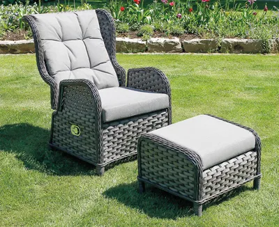 A gray wicker garden chair and ottoman are set up on a green lawn with a flower bed in the background.