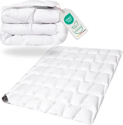 A folded duvet is shown stacked on top of itself, with a separate, unfolded duvet laid out below it. A tag with certifications is attached to the folded duvet.