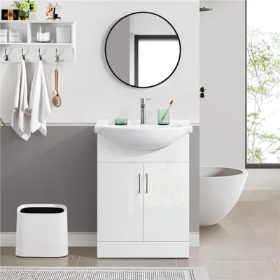 A modern bathroom vanity with a sink and cabinet, a round mirror above, and towels hanging on a shelf.