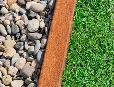 A close-up view of a garden border made of Corten steel, separating gravel from grass.