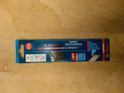 A Bosch Expert Thick Tough Metal reciprocating saw blade in its packaging, lying on a wooden surface.