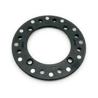 A black circular object with small silver magnets embedded around its edge, on a white background.