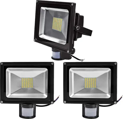 Three black LED floodlights with motion sensors are displayed against a white background. One floodlight is positioned above and to the right of the other two, which are side-by-side.