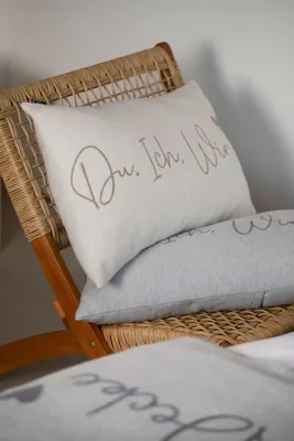 Two pillows are placed on a wicker chair, with a blanket in the foreground.