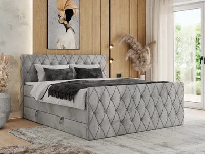 A bedroom scene featuring a large, upholstered boxspring bed with storage drawers, set against a wood-paneled wall and a large window.