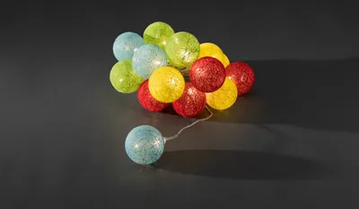 A cluster of colorful cotton ball string lights on a dark gray background.
