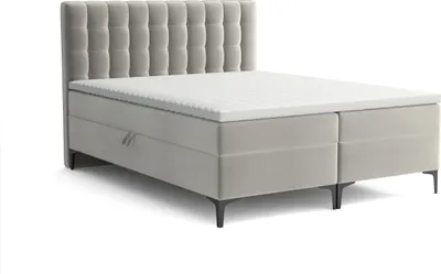 A studio shot of a gray boxspring bed with a tufted headboard and a white topper.