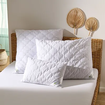 Several white pillows of different sizes are arranged on a white bed with a wicker headboard.
