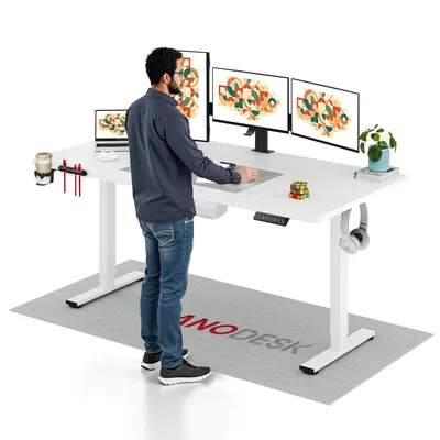 A man is standing at a white standing desk with multiple monitors, a laptop, and office accessories.