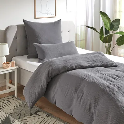 A bed with grey bedding, pillows, and a bedside table with a lamp and decorative items.