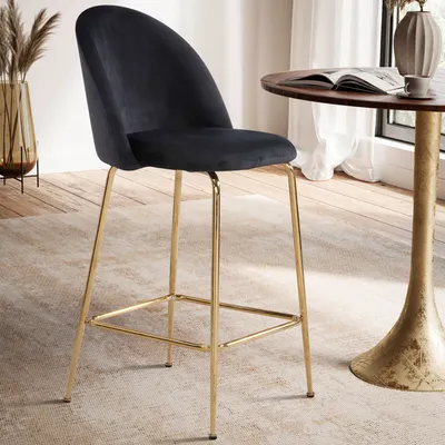 A black velvet bar stool with gold legs is placed next to a small round table in a well-lit room.