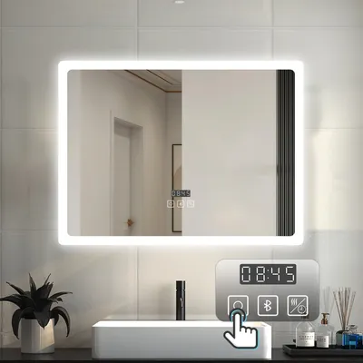 A modern bathroom sink with a large LED mirror above it. The mirror displays the time and has touch controls. A plant and toiletries are visible on the counter.