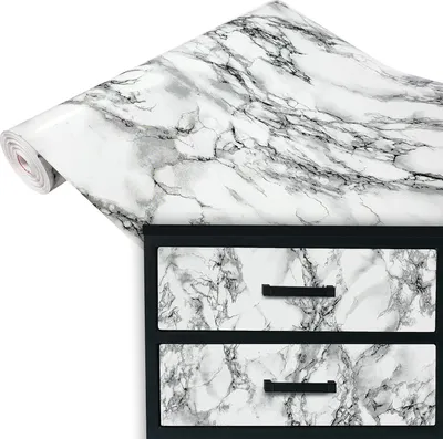 A roll of marble-patterned contact paper draped over a chest of drawers with matching marble-patterned drawer fronts.