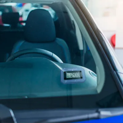 A digital parking disc is mounted on the dashboard of a car, visible through the windshield.
