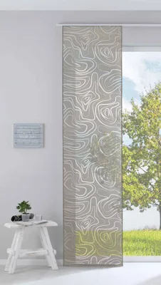 A panel curtain with a swirling pattern hangs in front of a window with a view of a tree and grass. A small white stool with a plant and a book sits to the left of the curtain.