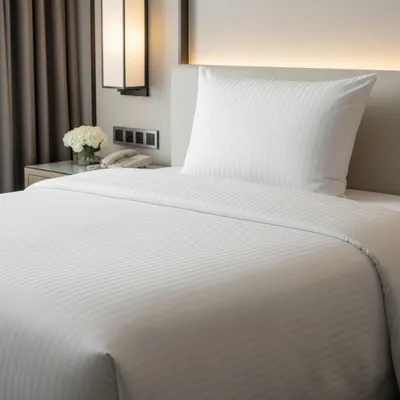 A neatly made hotel bed with white striped bedding and a pillow.