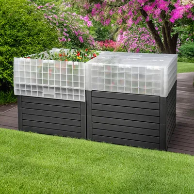Two raised garden beds with greenhouse tops are shown in a garden setting with lush green grass and flowering bushes in the background.