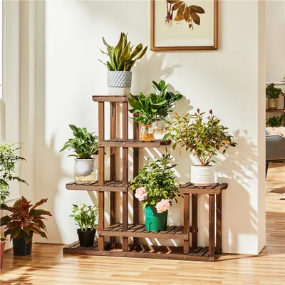 A wooden plant stand with multiple tiers filled with various potted plants, placed indoors near a wall and window.