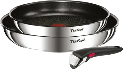 Two stacked stainless steel frying pans with a detachable handle in the foreground.