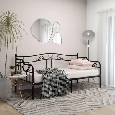A bedroom scene with a metal daybed, pillows, a blanket, a plant, and decorative mirrors.