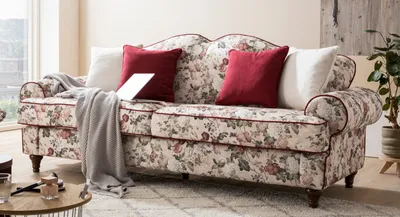 A floral patterned sofa with decorative pillows and a throw blanket, placed in a living room setting.