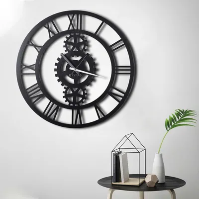 A large, black, metal wall clock with Roman numerals and visible gears is mounted on a white wall.