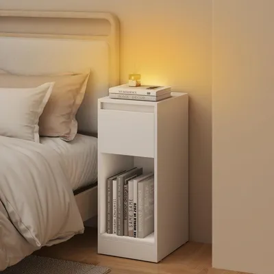 A white bedside table with books and a small decorative item is placed next to a bed.