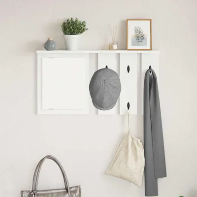 A white wall-mounted coat rack with a shelf above it, displaying a plant, a framed picture, a cap, a scarf, and a bag.