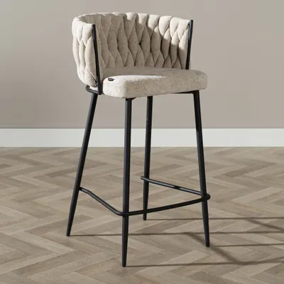 A bar stool is shown in a studio setting against a plain wall and on a wooden floor.