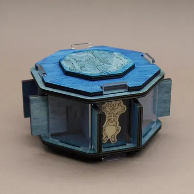 Jailbreak Geheimfach: blaue achteckige Holzbox mit Zahnrad-Deckel und graviertem Skelett hinter Acrylglasfach.