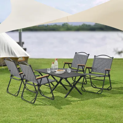 A camping table and chairs set is set up on a grassy area near a body of water, with a tent and canopy in the background.