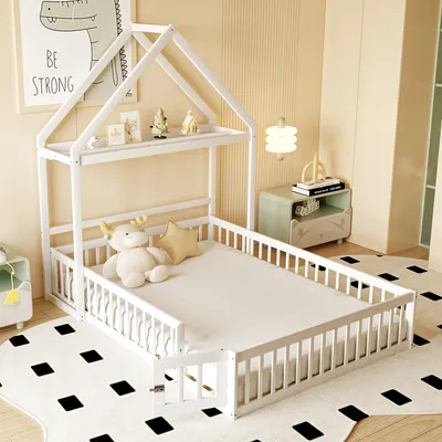 A white wooden house-shaped bed with a mattress, a stuffed reindeer, and a star pillow on it, placed in a child's bedroom with a patterned rug.