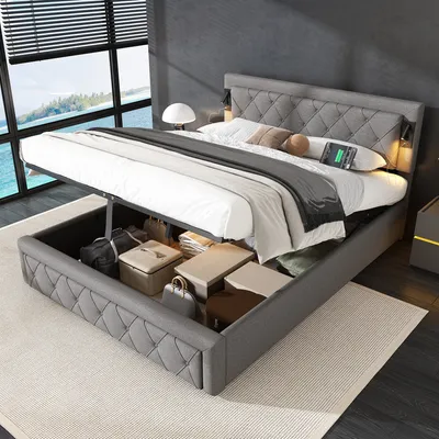 A bed with its storage compartment open, revealing various items stored inside. The bed is in a bedroom setting with a large window overlooking a body of water.