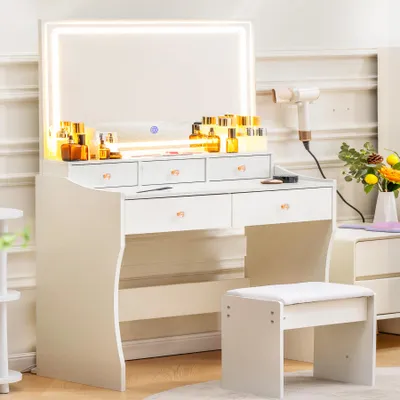 A white vanity table with a lighted mirror, drawers, and a stool, set in a room.