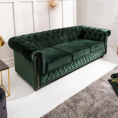 A dark green velvet Chesterfield sofa is shown in a well-lit room with a white paneled wall and a grey rug.