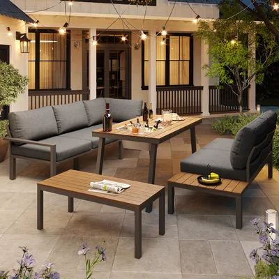 An outdoor patio scene at dusk, featuring a modular outdoor sofa set with a coffee table and a side table. String lights are visible overhead, and plants are in the foreground.