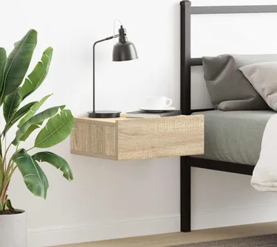 A floating nightstand next to a bed with a lamp and a cup on it.
