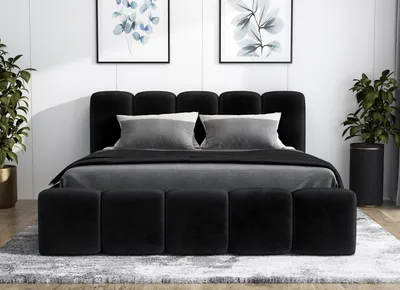 A black upholstered bed with a headboard and a bench at the foot of the bed, set in a bedroom with artwork on the wall and plants.