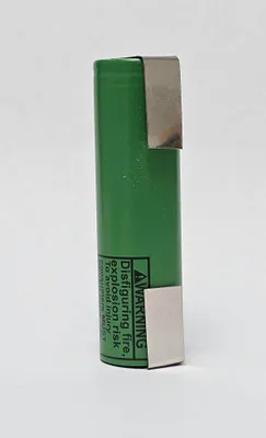 A single green cylindrical battery with silver metal clips on the top and bottom. There is warning text on the side of the battery.