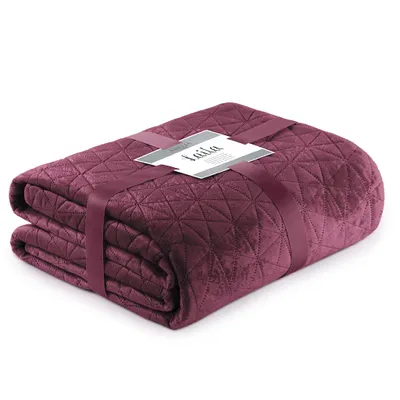 A folded quilted blanket with a geometric pattern, tied with a ribbon and a tag.
