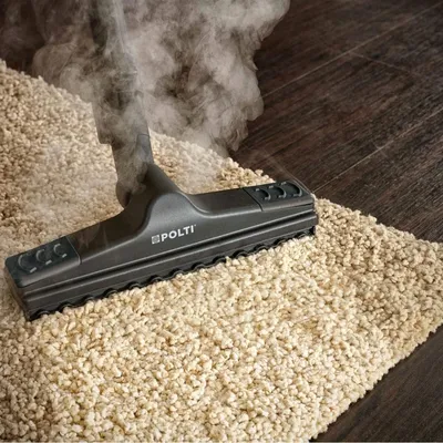 A steam cleaner head is shown cleaning a beige carpet next to a dark wood floor.