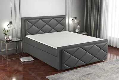 A dark gray boxspring bed with a diamond-stitched headboard and footboard, set up in a bedroom with a nightstand and lamp.
