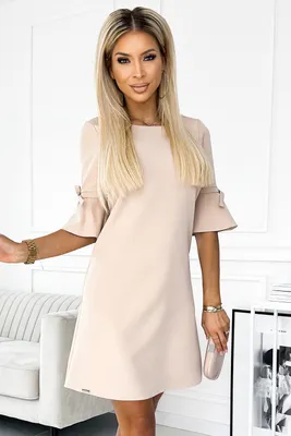 A woman wearing a beige dress stands in a room.