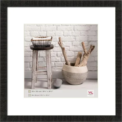 A framed picture of a stool with a basket on top and a pot with branches next to it, set against a brick wall.