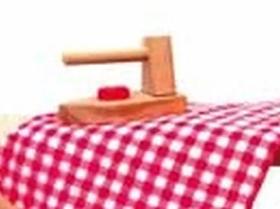 A wooden toy iron sits on a red and white checkered fabric, likely a tablecloth or ironing board cover.