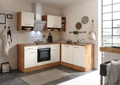 A modern kitchen setup with white and wood-tone cabinets, a stove, and a sink, set against a white brick wall and a large window.